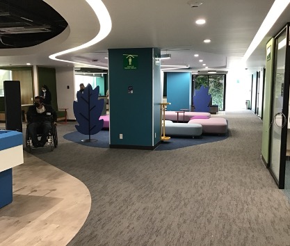 La imagen muestra una oficina donde una persona en silla de ruedas se desplaza con facilidad. El piso es de color café y tiene una textura de alfombra. Se ven sillones bajos de color azul y rosa. Las paredes son coloridas, creando un ambiente armonioso y accesible. Hay una iluminación adecuada proporcionada por las luces, y se pueden ver puertas de vidrio corredizas que conducen a otra oficina.
La imagen muestra de manera panorámica una zona amplia con edificaciones. Se destacan cuatro edificios muy grandes rodeados de vegetación, árboles y albercas, lo que le da una apariencia de zona residencial. A los lados se pueden ver más edificaciones
